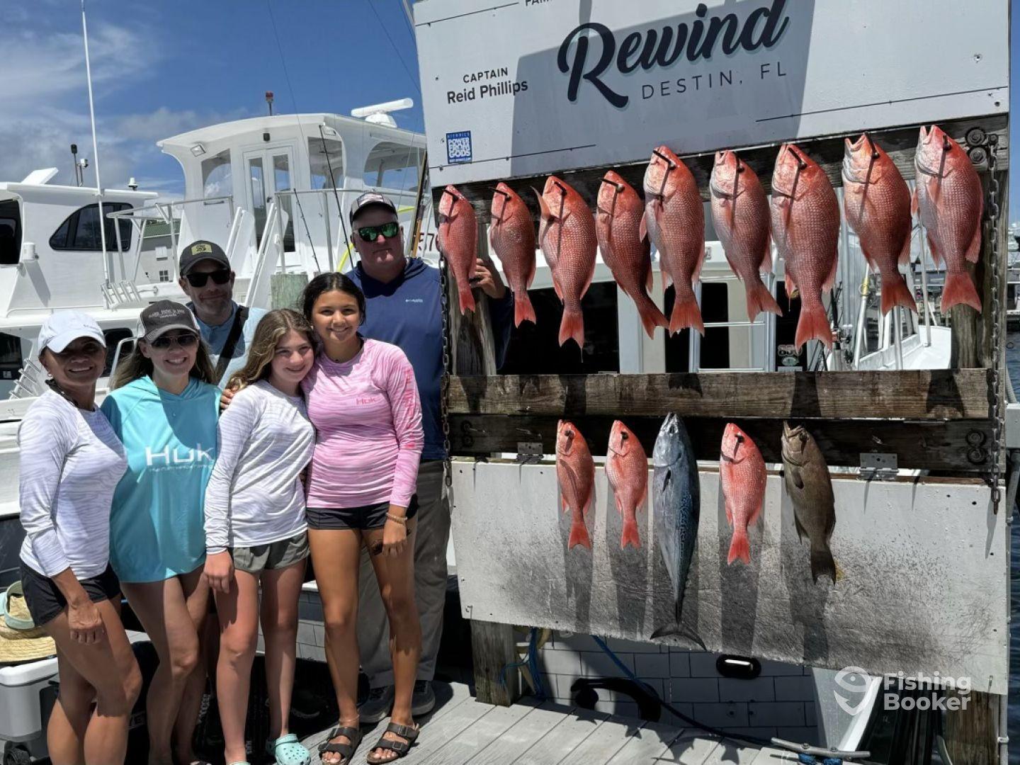 A family poses proudly in front of a catch board displaying an impressive haul of Red Snapper and a Mackerel after a successful fishing trip in Destin, FL.
