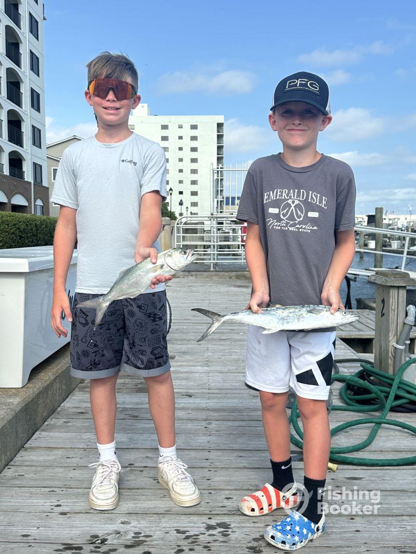 Two young anglers proudly displaying their catches, a Spanish Mackerel and a Bluefish, at the dock after a successful fishing trip.