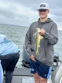 A young angler proudly displaying a Walleye while fishing on a boat, showcasing a typical day on the water.