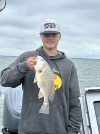 Young angler proudly holding a sizable fish while fishing on a boat, showcasing a successful catch in a scenic waterway.