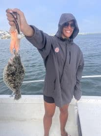 An angler proudly displaying a Flounder while fishing from a boat, showcasing a successful catch in a coastal environment.