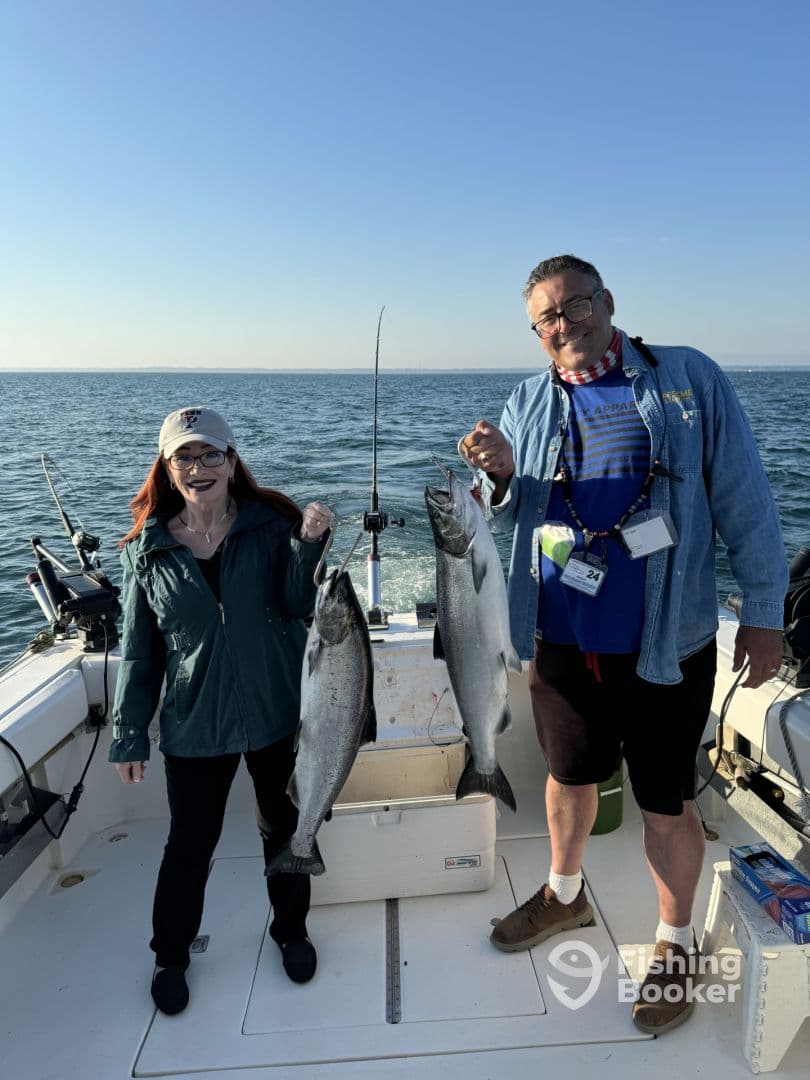 Two anglers proudly displaying their catch of Chinook Salmon aboard a fishing boat in open waters.