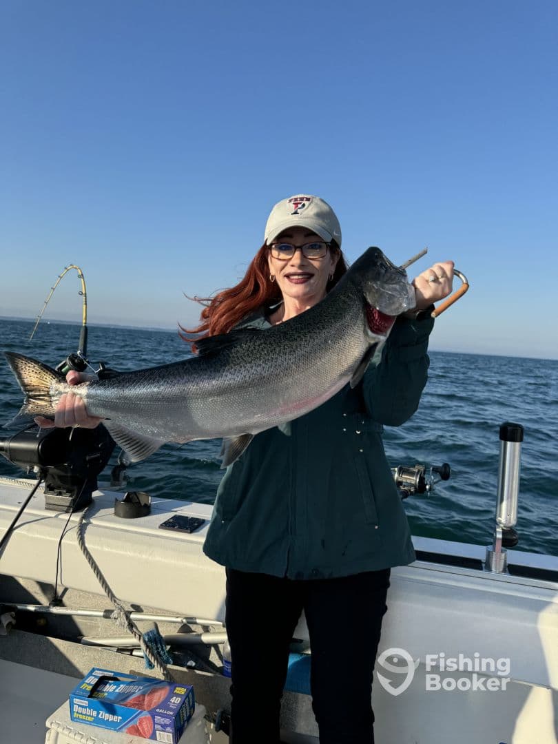 An angler proudly displaying a large Rainbow Trout while fishing on a boat in clear waters.
