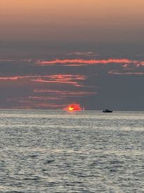 A picturesque sunset over the ocean with a small fishing boat silhouetted against the vibrant sky.