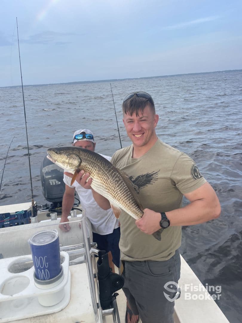 Angler proudly displaying a large Redfish while fishing on a boat, showcasing a successful day on the water.