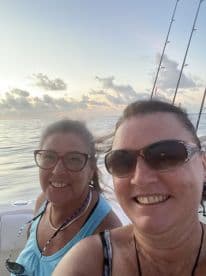 Two women enjoying a sunset selfie on a fishing boat, with calm waters in the background.