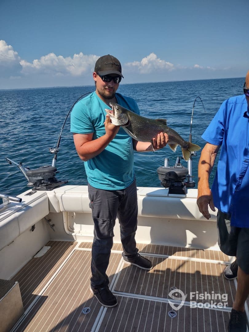 Angler proudly displaying a large Lake Trout aboard a fishing boat, enjoying a day on the open water.