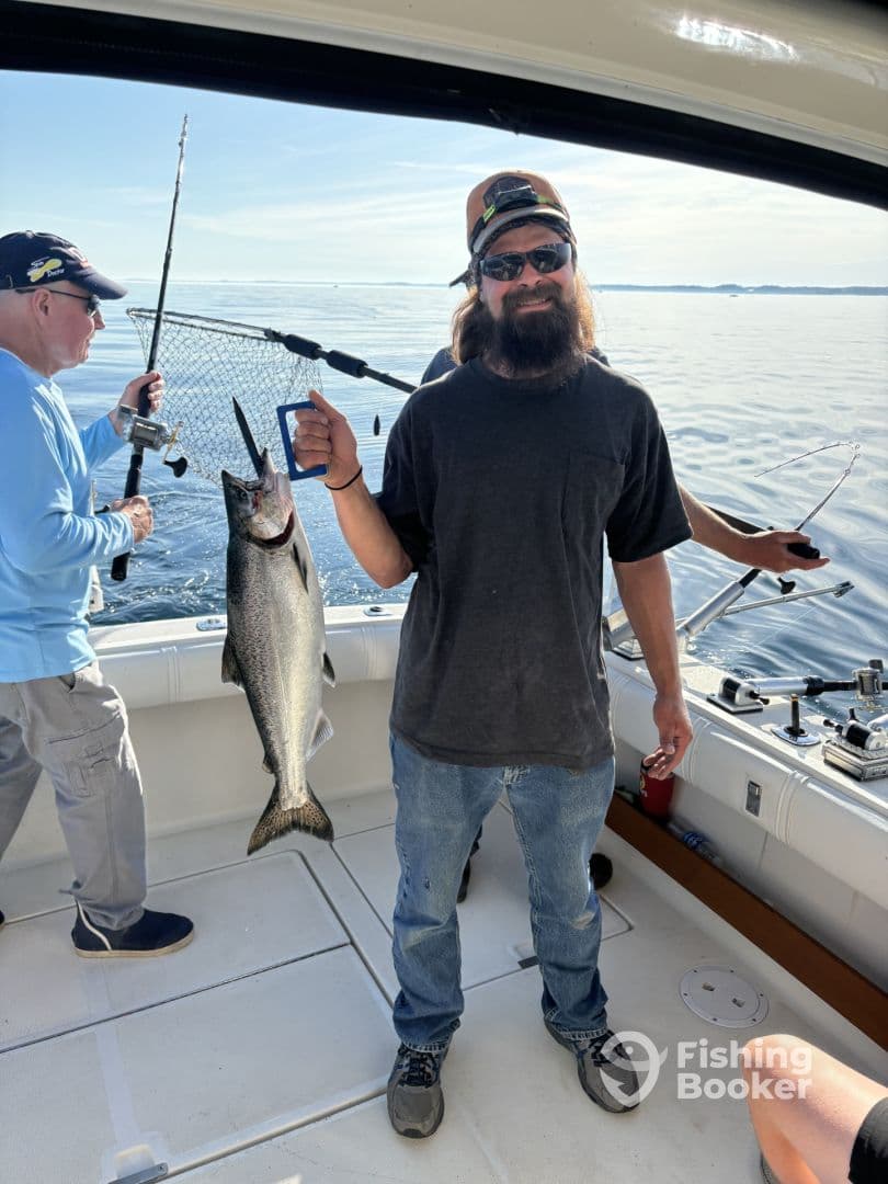 Angler proudly displaying a large Salmon while fishing on a boat, with calm waters in the background.