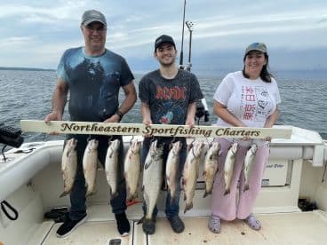 A family proudly displaying their catch of trout on a fishing charter, showcasing a successful day on the water.