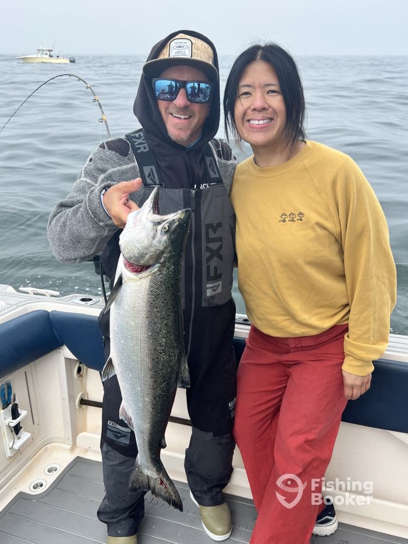Two anglers proudly displaying a large Salmon on a fishing boat, showcasing a successful day on the water.