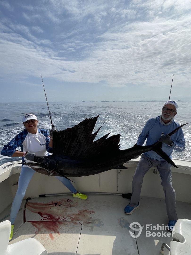 Two anglers proudly displaying a large Sailfish on a fishing charter in open waters, showcasing their successful catch.