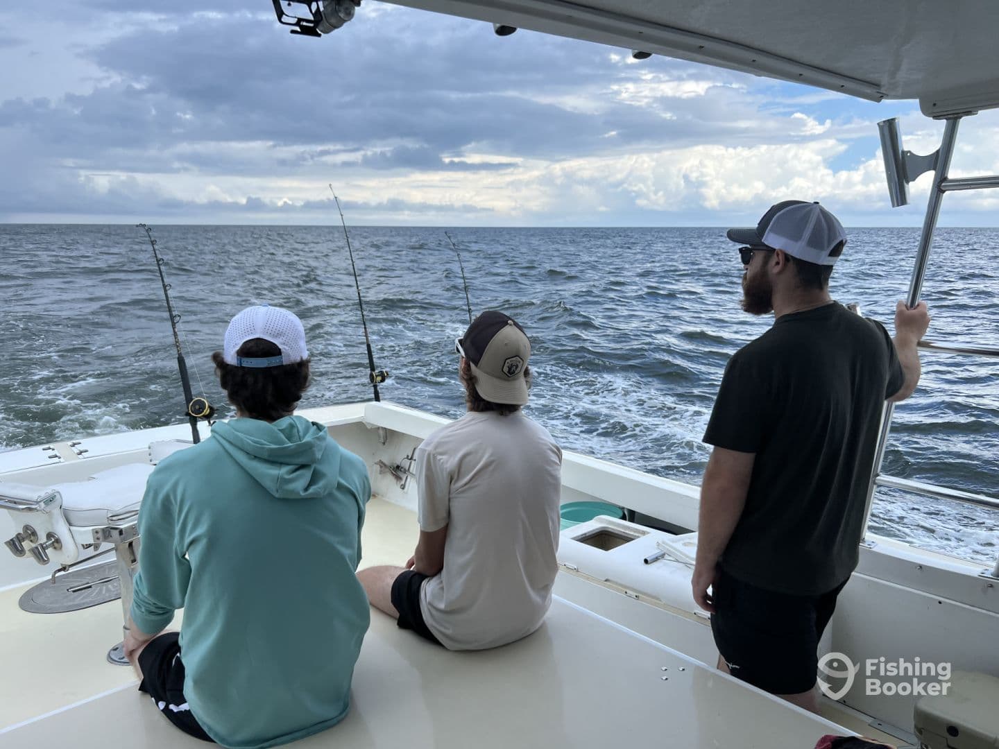 Three anglers on a fishing boat, focused on the water as they await a catch during a deep-sea fishing trip.