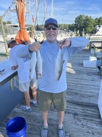 An angler proudly displaying three Spanish Mackerel at the dock after a successful fishing trip.