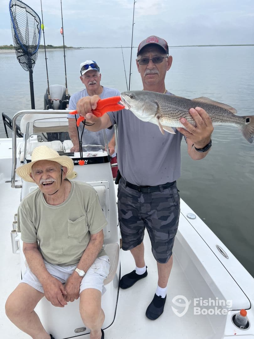 A group of anglers enjoying a fishing trip, with one proudly displaying a large Redfish caught from a boat.