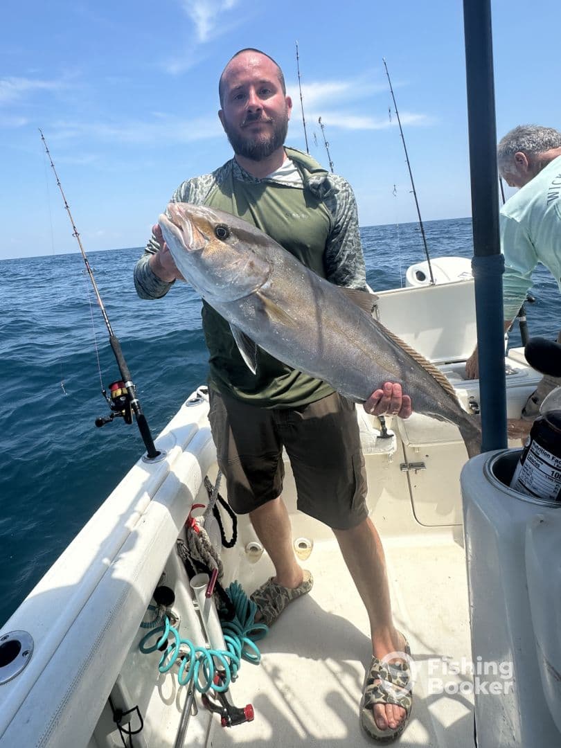 An angler proudly displaying a large Amberjack aboard a fishing boat in open waters.