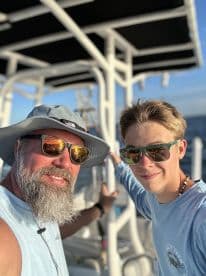 A father and son duo enjoying their time aboard a fishing charter, showcasing the boat's interior and a sunny day on the water.