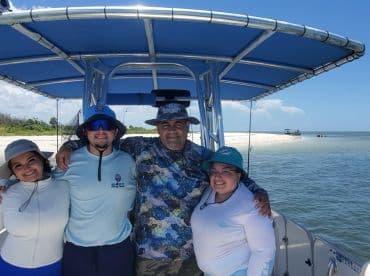 A group of four friends enjoying a day on a fishing boat, showcasing a sunny day on the water with a beautiful backdrop.