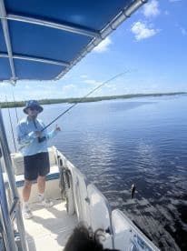 A young angler is reeling in a fish while fishing from a boat in a calm waterway, showcasing an engaging fishing experience.