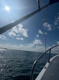 A scenic view from the side of a boat, showcasing the bright sun and clear blue skies over calm waters, ideal for a fishing adventure.