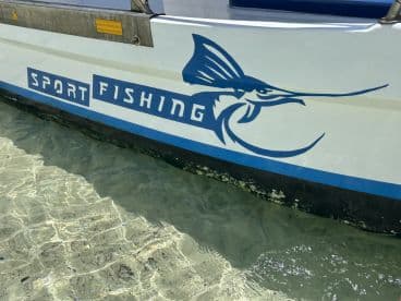 The exterior of a sport fishing boat featuring a marlin graphic, anchored in clear waters, showcasing a vibrant fishing environment.