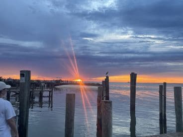 A serene sunset view over the water with a silhouette of a person walking along the dock, creating a peaceful fishing atmosphere.