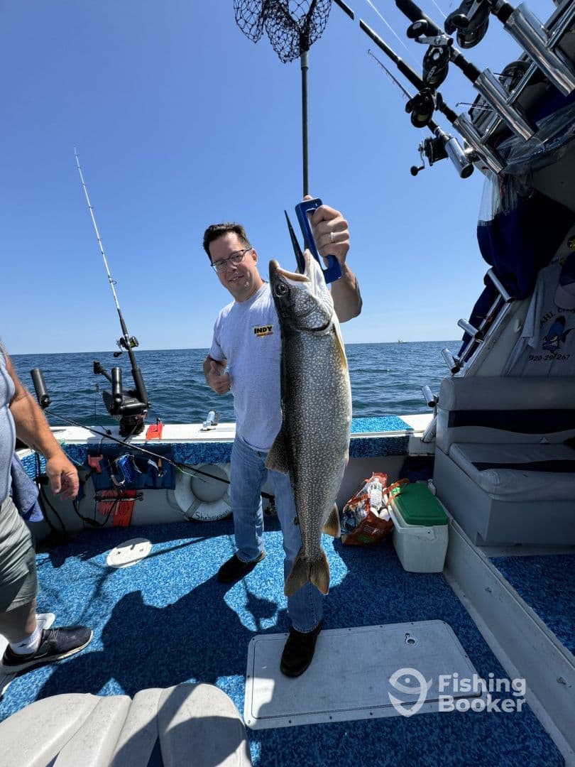 An angler proudly displaying a large Lake Trout aboard a fishing boat, showcasing a successful day on the water.