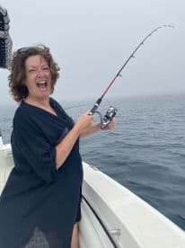 A woman enthusiastically reeling in a catch while fishing on a foggy day, showcasing the excitement of the sport.