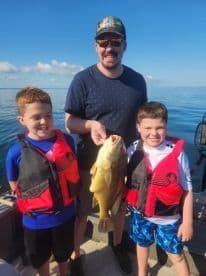 A proud father and his two sons display a large Largemouth Bass while fishing on a sunny day.