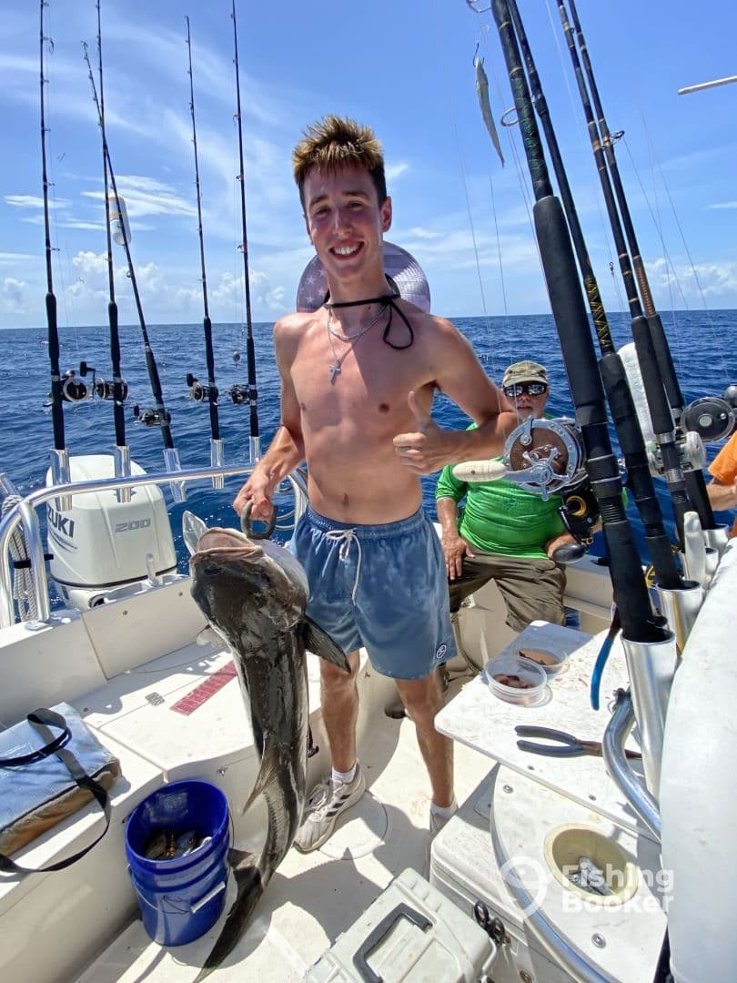 A young angler proudly displaying a large Black Grouper while fishing on a sportfishing boat in open waters.