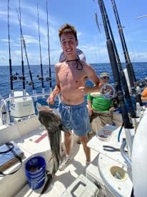 A young angler proudly displaying a large Black Grouper while fishing on a sportfishing boat in open waters.