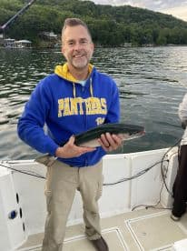 An adult angler proudly displaying a freshly caught trout while fishing on a serene lake, surrounded by lush greenery.