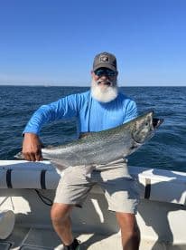 An angler proudly displaying a large Salmon while fishing on a sunny day, showcasing the excitement of a successful catch.