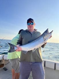 Angler proudly displaying a large Salmon while fishing on a boat in open waters.