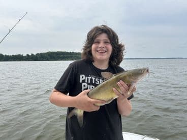 A young angler proudly displaying a large catfish while fishing on a lake, showcasing a successful day on the water.