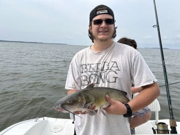 A young angler proudly displaying a large Catfish while fishing on a boat, showcasing a successful day on the water.
