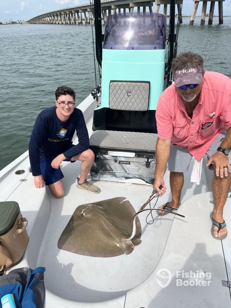 A young angler and an experienced fisherman displaying a large stingray on a boat, showcasing a successful catch during a fishing trip.