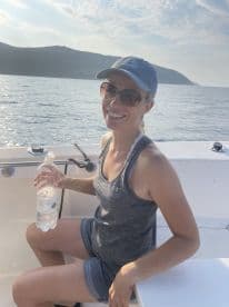 A woman enjoying her time on a boat, holding a water bottle, with scenic views of the water and mountains in the background.