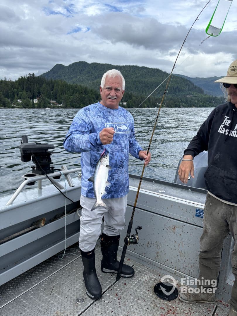 An angler proudly displaying a freshly caught fish while fishing on a scenic lake surrounded by mountains.