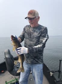 An angler proudly displaying a Walleye while fishing on a calm lake, showcasing the thrill of freshwater fishing.