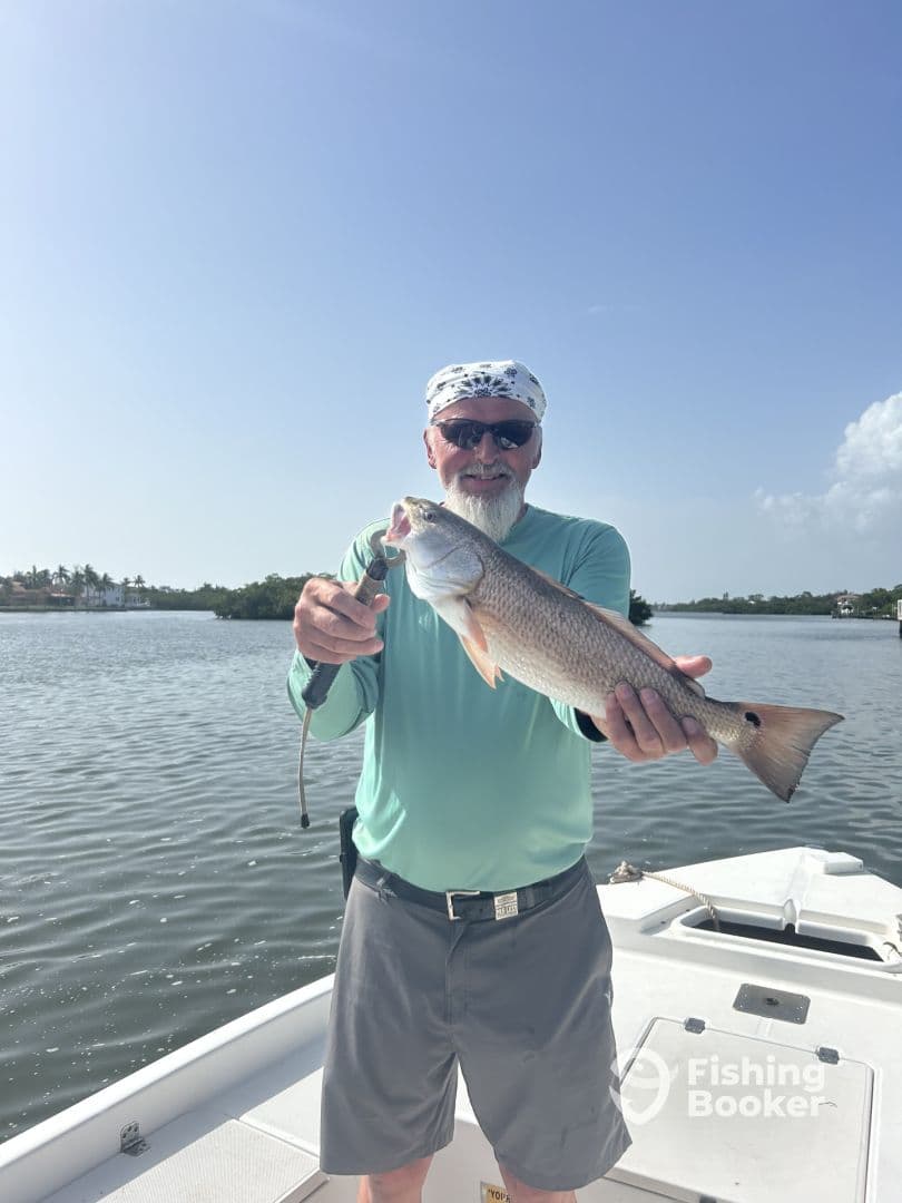 An angler proudly displaying a Redfish while fishing on a boat in a calm waterway.