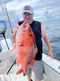 An angler proudly displaying a large Red Snapper while fishing offshore, showcasing the vibrant colors of the catch against a scenic ocean backdrop.