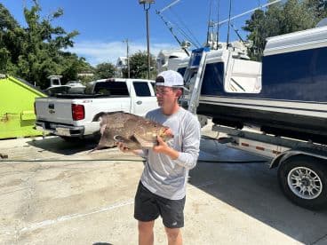 Young angler proudly holding a large Grouper at the dock after a successful fishing trip.