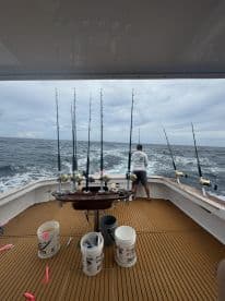 A fisherman stands at the back of a sportfishing boat, preparing for action with multiple fishing rods set up on the deck, showcasing a well-equipped fishing environment.
