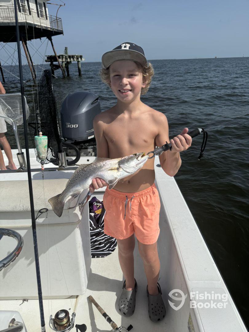 A young angler proudly displaying a large Speckled Trout while fishing from a boat in coastal waters.