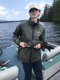 Young angler holding a large Largemouth Bass while fishing on a serene lake, surrounded by lush greenery.
