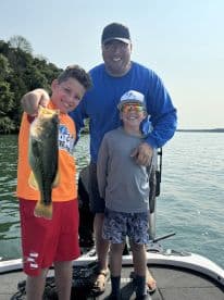 A young angler proudly displaying a large Largemouth Bass while enjoying a day of fishing with family on a lake.