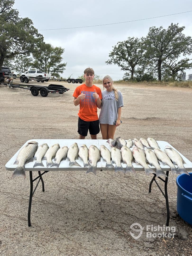 Two young anglers proudly displaying a catch of striped bass on a table after a successful fishing trip.