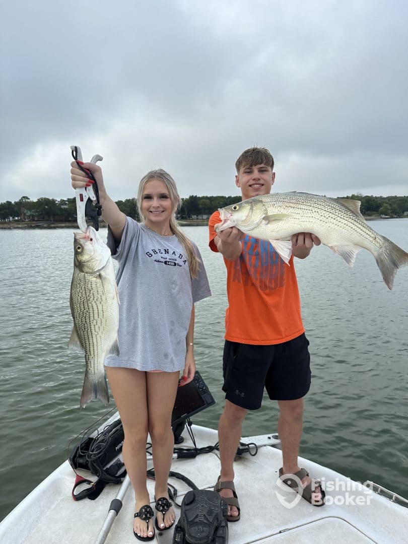 Two young anglers proudly displaying their catch of striped bass while on a boat, showcasing a successful day on the water.