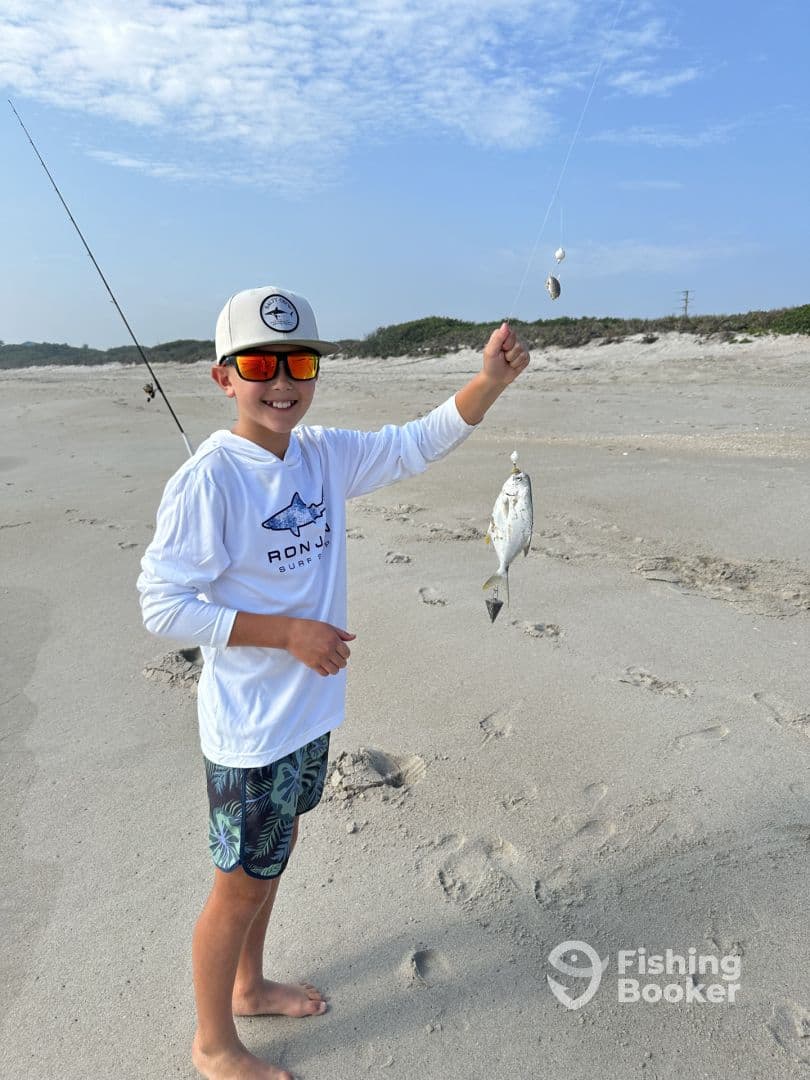 A young angler proudly displaying a caught fish on the beach, showcasing a fun day of surf fishing.
