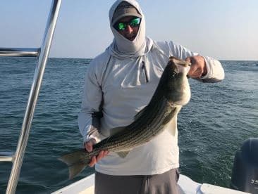 Angler proudly displaying a large Striped Bass while fishing on a boat in open waters.